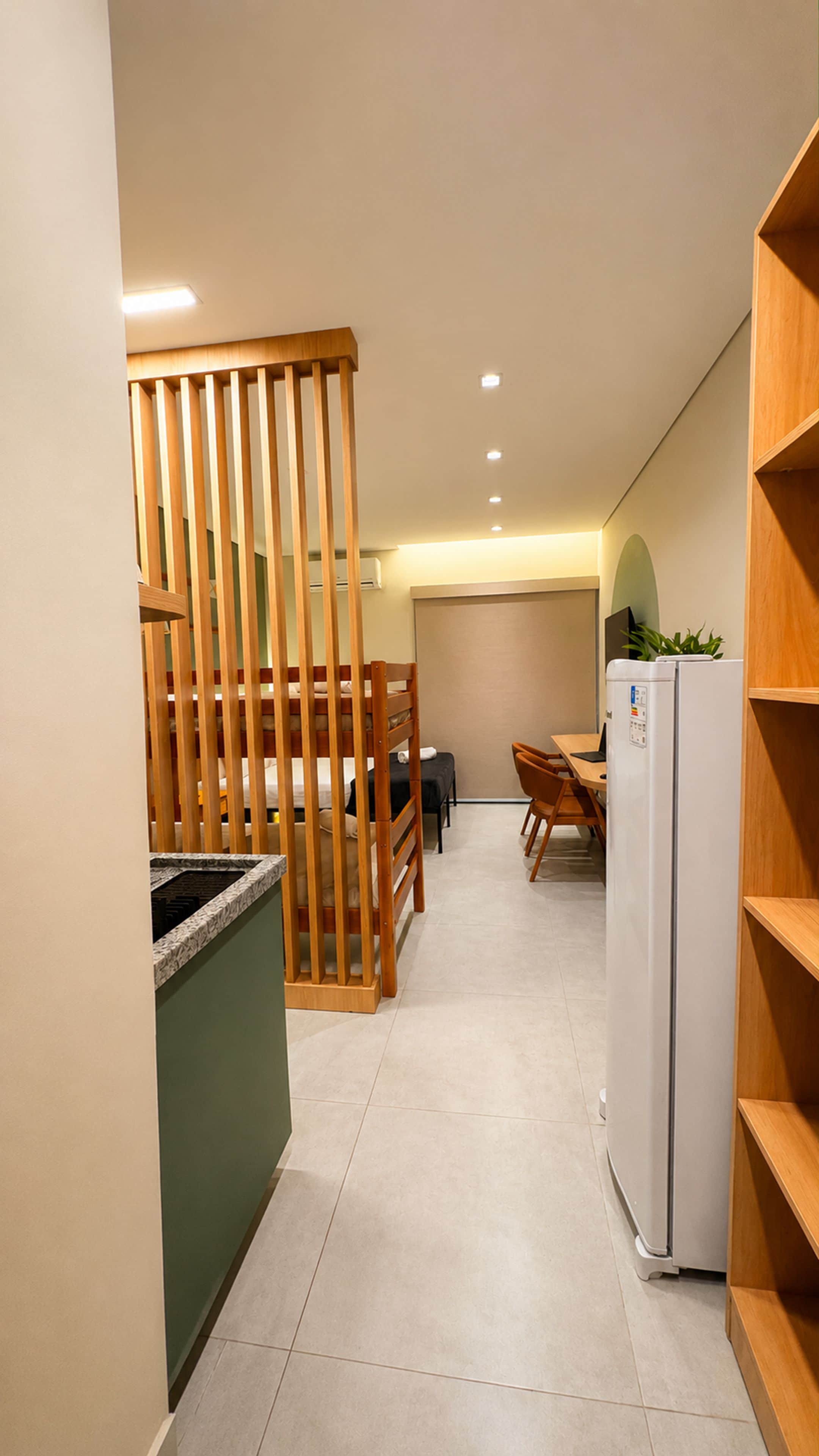 A narrow hallway with a wooden partition, a dining area with a table and chairs, and a white refrigerator.