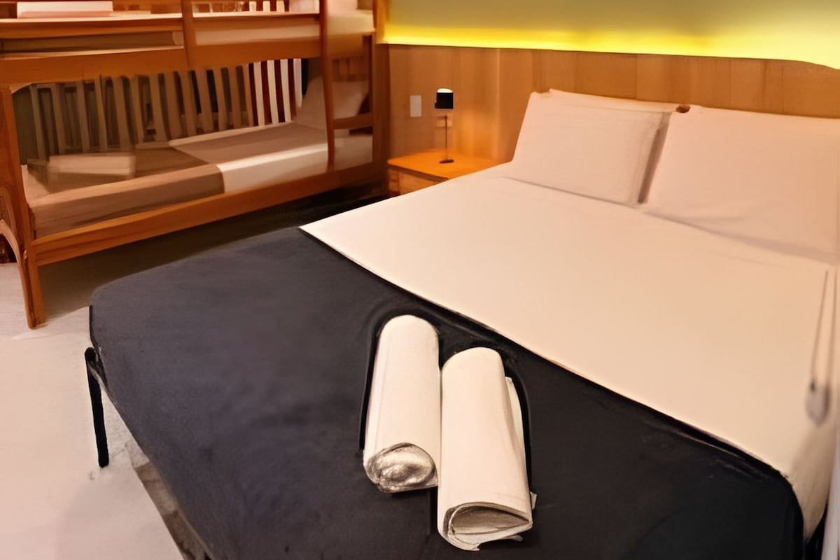 A hotel room with a bed, a wooden bench, and a wall-mounted paddleboard.