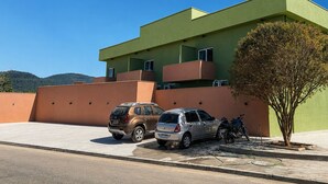 Un edificio moderno con techo plano, un árbol en primer plano y dos coches estacionados.
