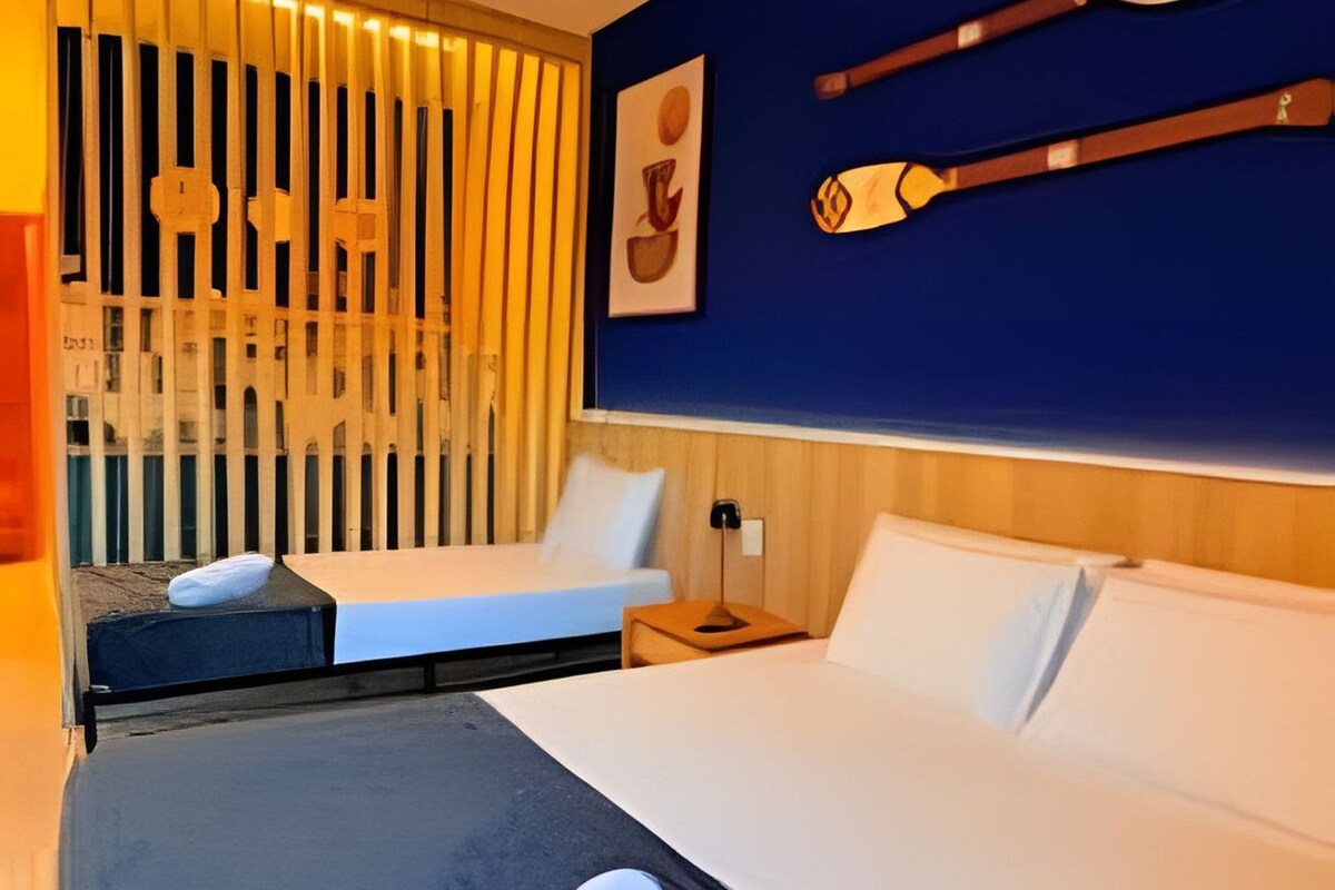 A hotel room with a bed, a desk, a chair, and a window with blinds.