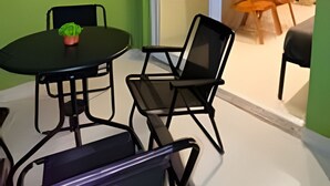 Una habitación con una mesa de comedor y sillas, una pequeña planta en maceta, y un ventanal corredero que da a otra habitación con un televisor.