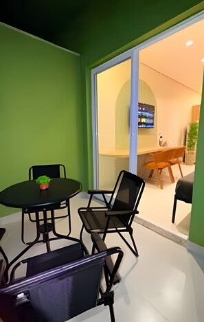 A room with a dining table and chairs, a small potted plant, and a sliding glass door leading to another room with a television.