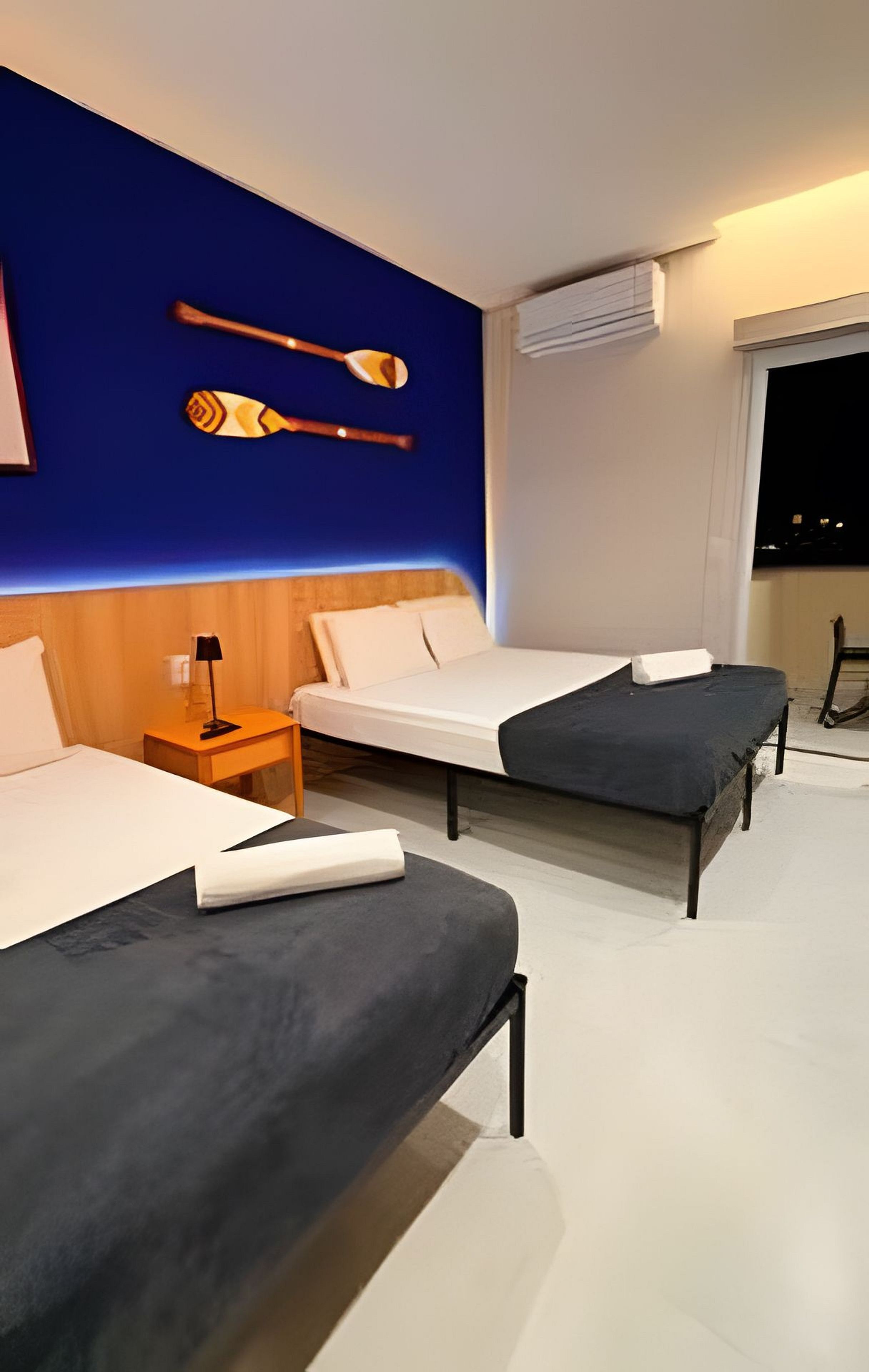 Une chambre d’hôtel avec deux lits, une table de chevet, une lampe et un climatiseur fixé au mur.