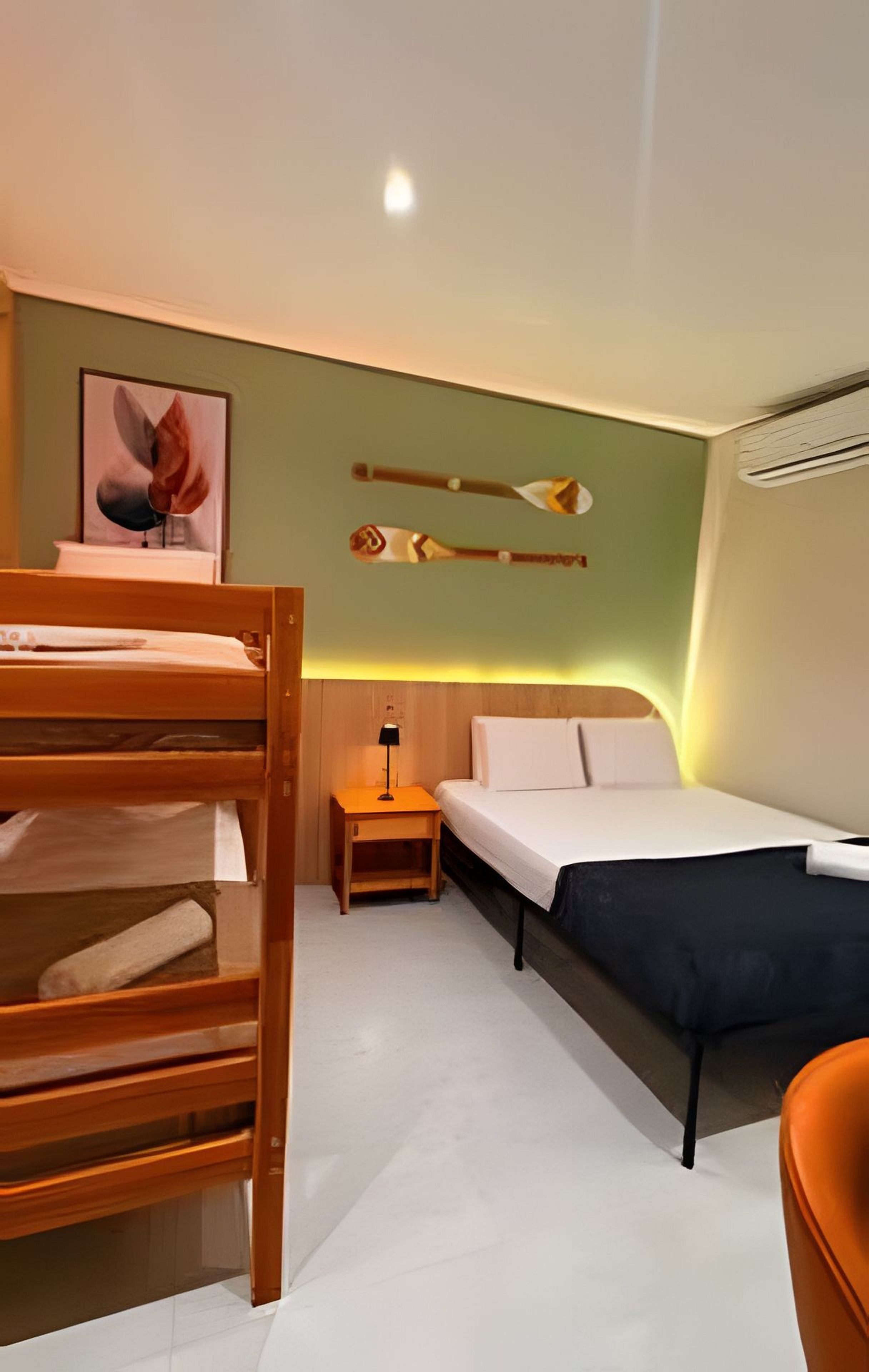 A hotel room with a bunk bed, a single bed, a nightstand with a lamp, and a wall-mounted shelf with decorative items.