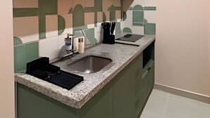 Cocina con encimera de granito, un lavamanos y una cafetera. Hay tres platos colgados en la pared sobre la encimera.