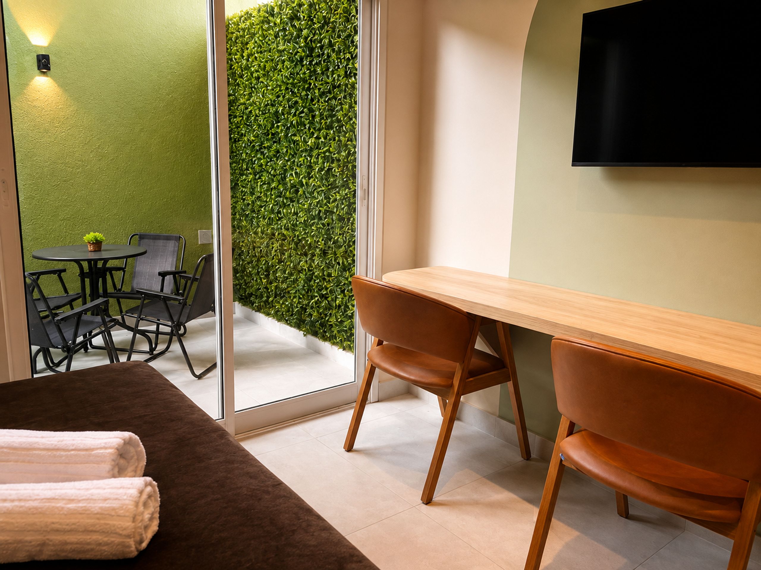 Une pièce moderne avec une table en bois, deux chaises, un canapé, un téléviseur à écran plat et un mur vert.