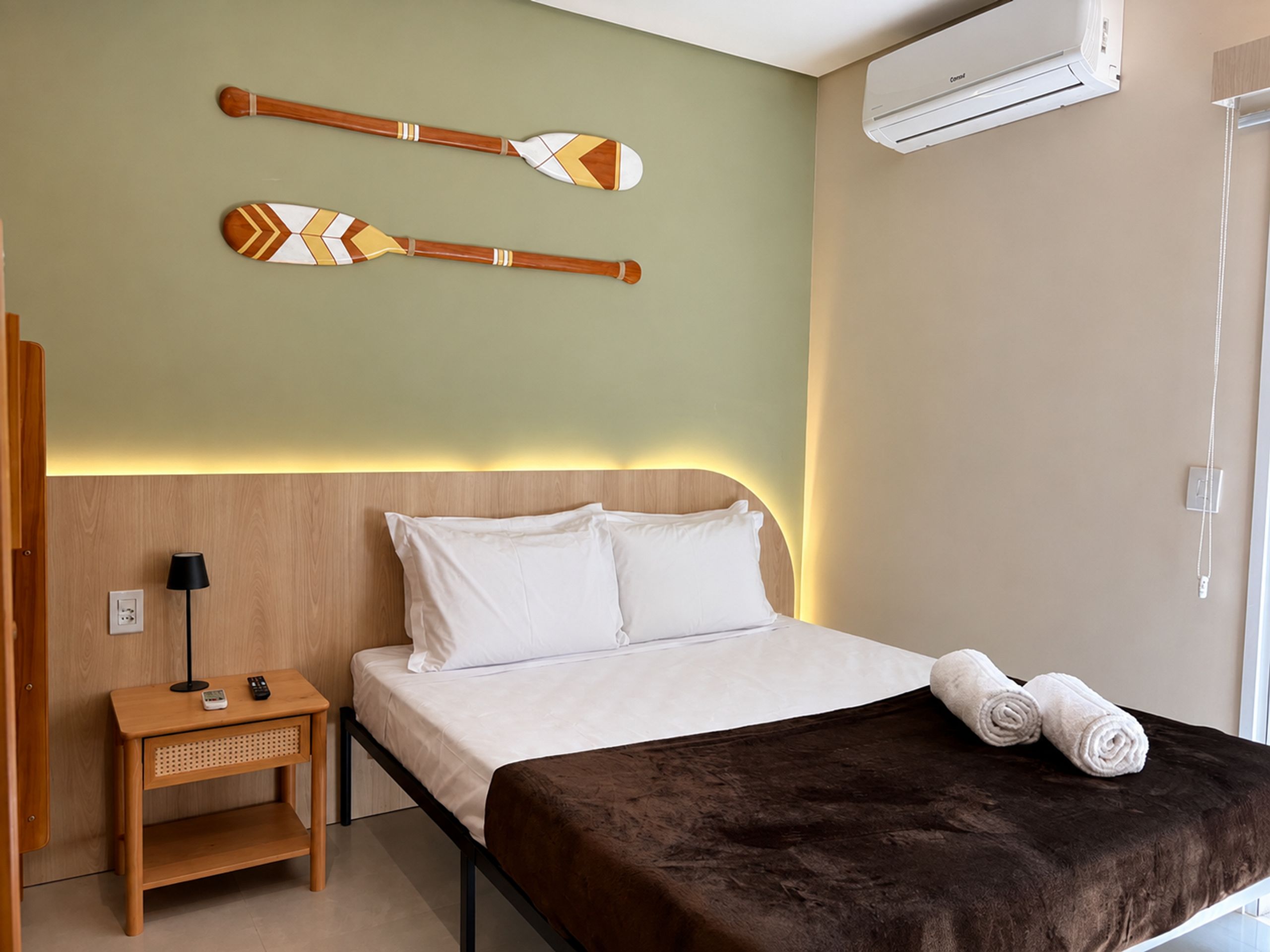 Habitación de hotel con cama, mesita de noche, lámpara, aire acondicionado instalado en la pared y decoración en la pared.