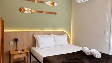 Habitación de hotel con cama, mesita de noche, lámpara, aire acondicionado instalado en la pared y decoración en la pared.