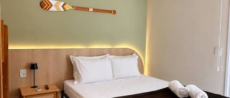 A hotel room with a bed, bedside table, lamp, wall-mounted air conditioner, and decorative wall art.