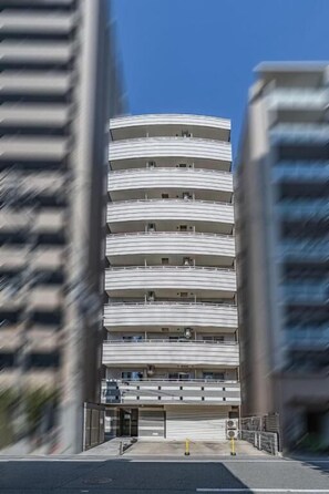 Ein mehrstöckiges Gebäude mit geschwungener Fassade, einem Eingang im Erdgeschoss und einem Parkbereich.