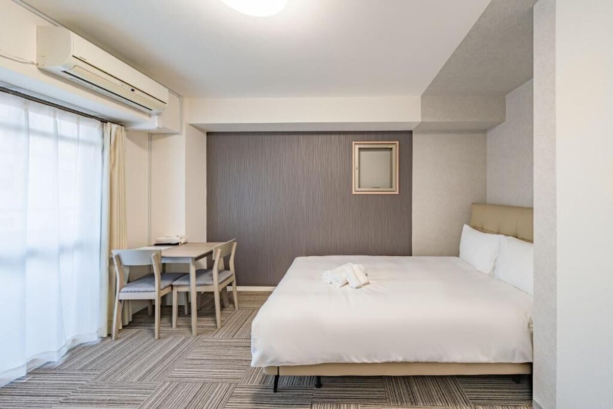 Ein Hotelzimmer mit einem Bett, einem Schreibtisch, einem Stuhl, einer Klimaanlage und einem fenster mit Vorhängen.