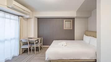 A hotel room with a bed, a desk, a chair, an air conditioning unit, and a window with curtains.