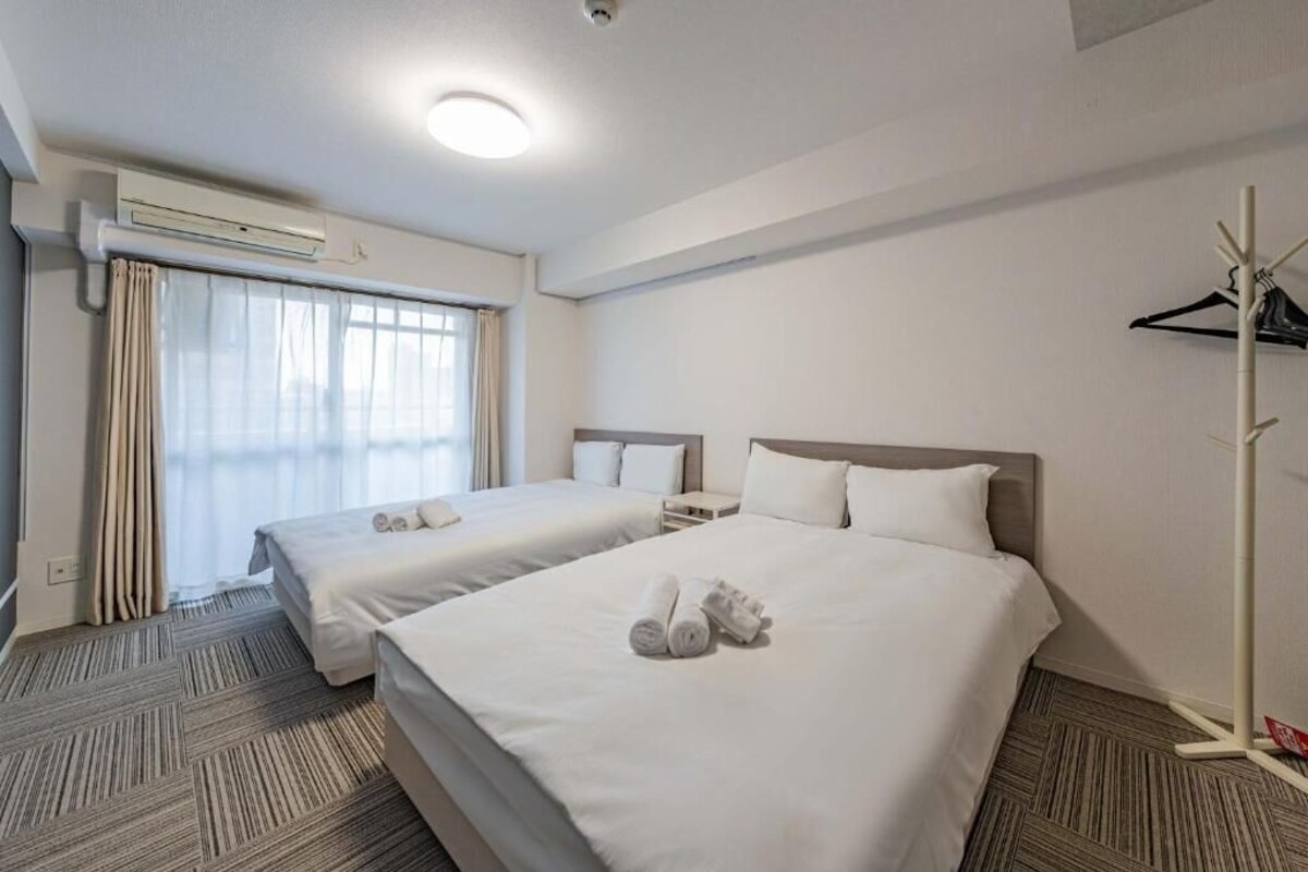 Ein Hotelzimmer mit zwei Betten, einem Fenster mit Vorhängen, einer Klimaanlage und einem Kleiderständer.