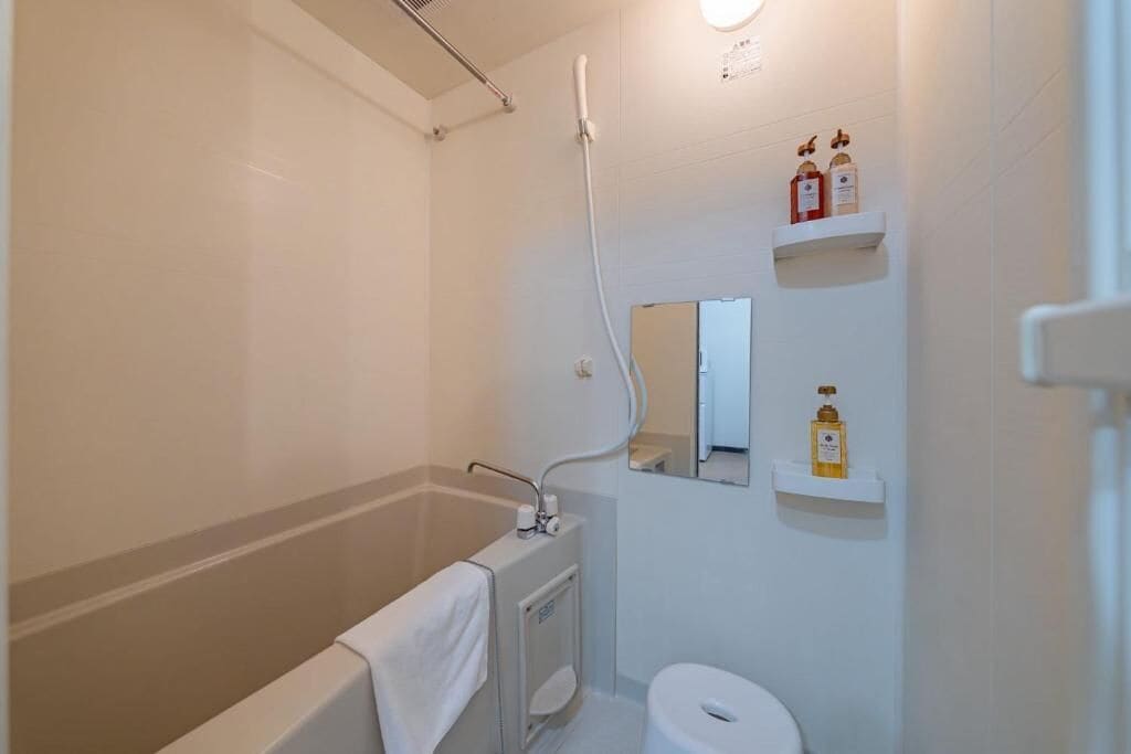 Un baño con bañera, inodoro, ducha y dos repisas con artículos de aseo.