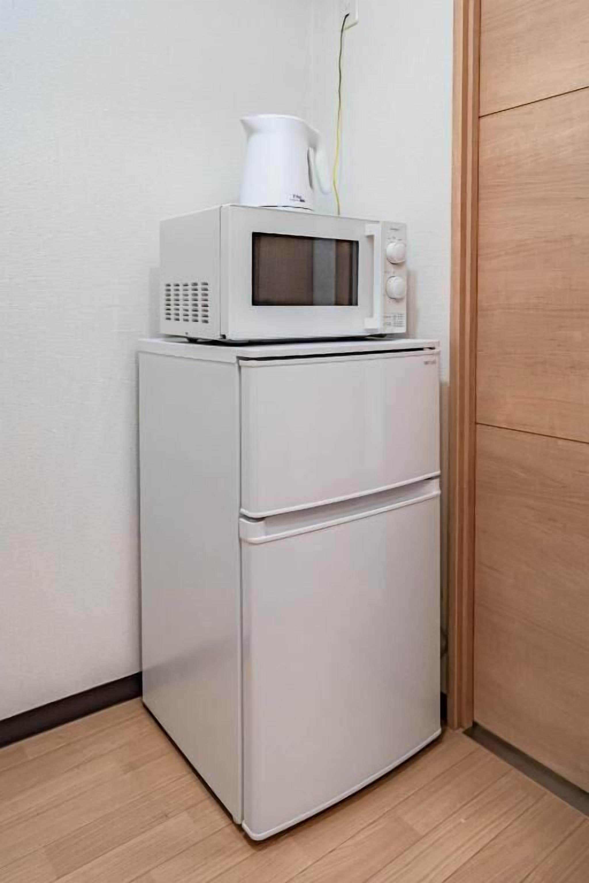 A white refrigerator with a microwave on top, a small white cabinet below, and a wooden door to the right.