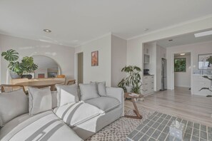 A modern living room with a sofa, a dining area with a table, and a kitchen with appliances. - Mount Nelson Lookout - 2 Bed House & Swimming Pool (Mount Nelson)
