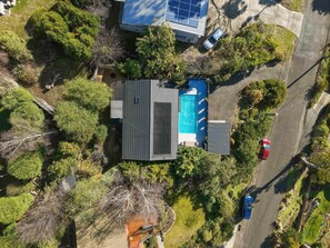 An aerial view of a residential area with a house featuring a swimming pool, solar panels, and a paved driveway. - Mount Nelson Lookout - 2 Bed House & Swimming Pool (Mount Nelson)