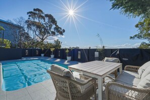 Ein Garten mit Swimmingpool, Korbmöbeln und blauem Himmel.