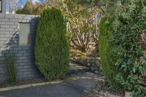 Ein Weg, gesäumt von ordentlich geschnittenen immergrünen Hecken, führt zu einer Steinmauer und einem Garten mit verschiedenen Pflanzen.