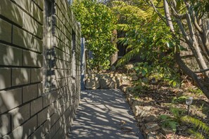 A narrow pathway flanked by a brick wall on one side and a stone wall with vegetation on the other. - Mount Nelson Lookout - 2 Bed House & Swimming Pool (Mount Nelson)