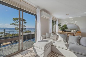 Ein Balkon mit Blick auf Meer und Berge, eine Couch mit Kissen und ein Blumentopf.