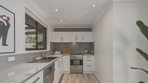 Cozinha moderna com armários brancos, eletrodomésticos de aço inoxidável e bancada de madeira.