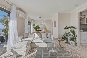 Ein modernes Wohnzimmer mit einem Ecksofa, einem kleinen runden Tisch und mehreren Blumentöpfen.