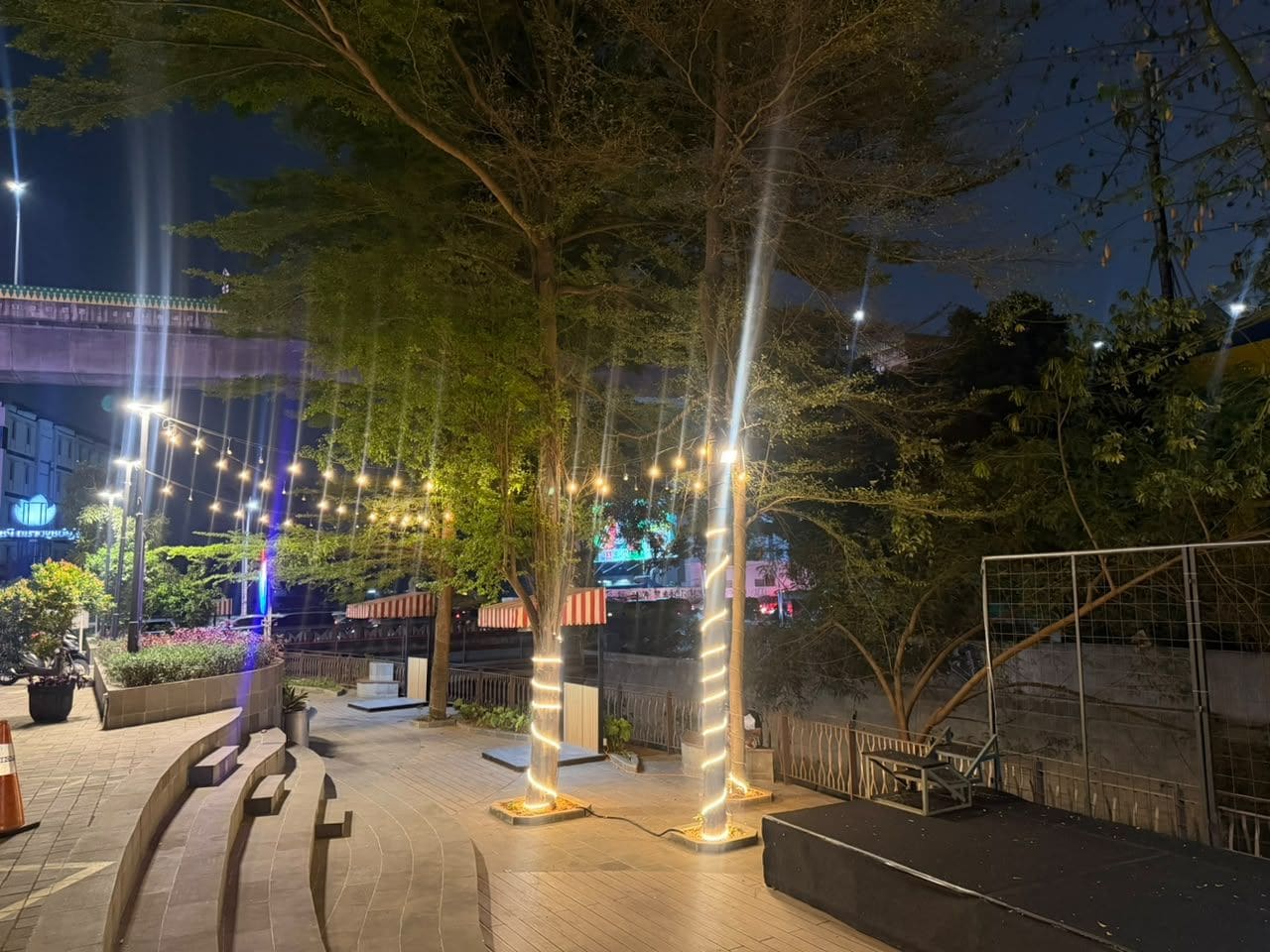 An outdoor area with trees, a paved walkway, and a fence.