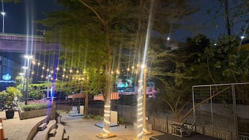 An outdoor area with trees, a paved walkway, and a fence.