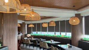 Interior de restaurante con mesas redondas, sillas y lámparas de mimbre colgantes.