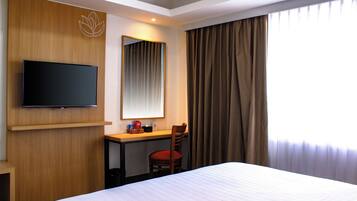 Una habitación de hotel con una cama, un escritorio, una silla, un televisor y una ventana con cortinas.
