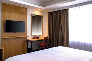 Ein Hotelzimmer mit einem Bett, einem Schreibtisch, einem Stuhl, einem Fernseher und einem Fenster mit Vorhängen.