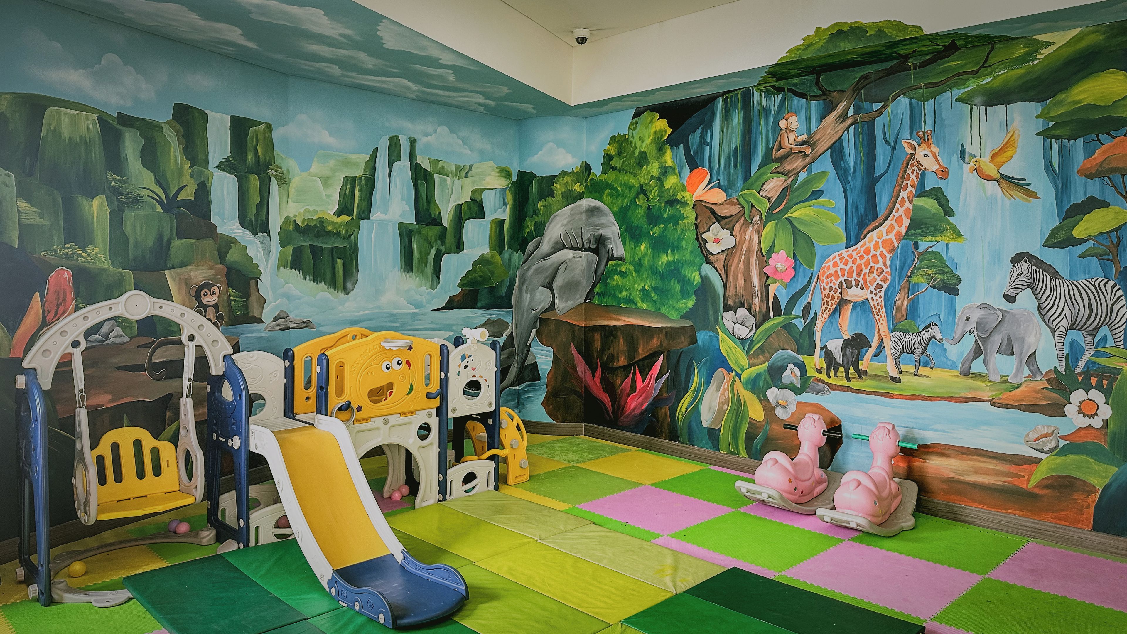 A children's play area with a slide, climbing structures, and a mural of jungle animals.