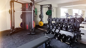 Un gimnasio con equipo de levantamiento de pesas, una banca y un espejo grande.