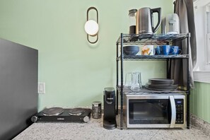 Una kitchenette con microondas, cafetera y una alacena con vajilla y tazas.