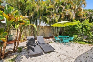 A patio area with two lounge chairs, a table, and a green umbrella. - Quiet Studio with Sunny Private Yard (Wilton Manors)