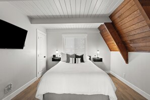 A bedroom with a sloped ceiling, a bed with white bedding, two bedside tables with lamps, and a wall-mounted TV. - Peaks View A-Frame: Hot Tub, Trails, A/C, andEV Charger (Flagstaff)