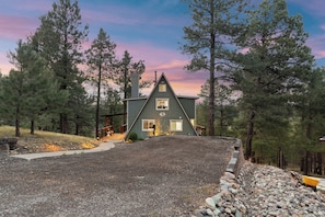 A two-story house with a steep roof, surrounded by trees and a gravel driveway. - Peaks View A-Frame: Hot Tub, Trails, A/C, andEV Charger (Flagstaff)