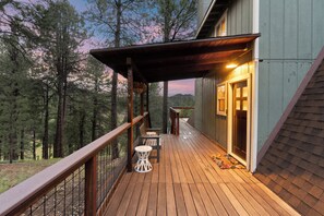 A wooden deck with a railing, a hanging flower basket, and a door leading to a building. - Peaks View A-Frame: Hot Tub, Trails, A/C, andEV Charger (Flagstaff)