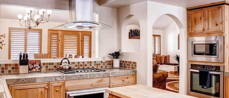 A modern kitchen with wooden cabinets, a gas stove, a microwave, and a large island with a kettle.