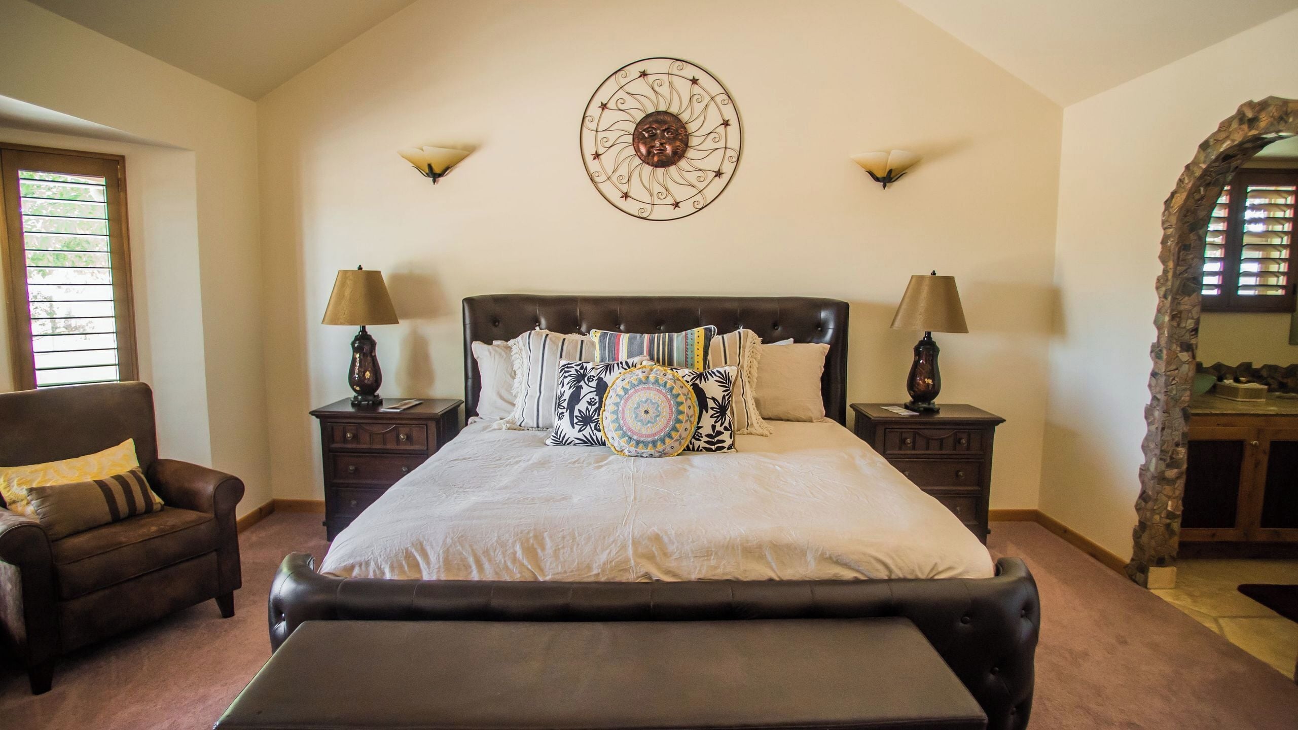 A bedroom with a large bed, two nightstands, a chair, and a decorative wall piece.
