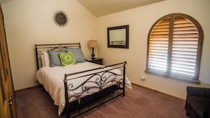 Un dormitorio con cama, mesita de noche, lámpara, espejo y ventana con persianas.