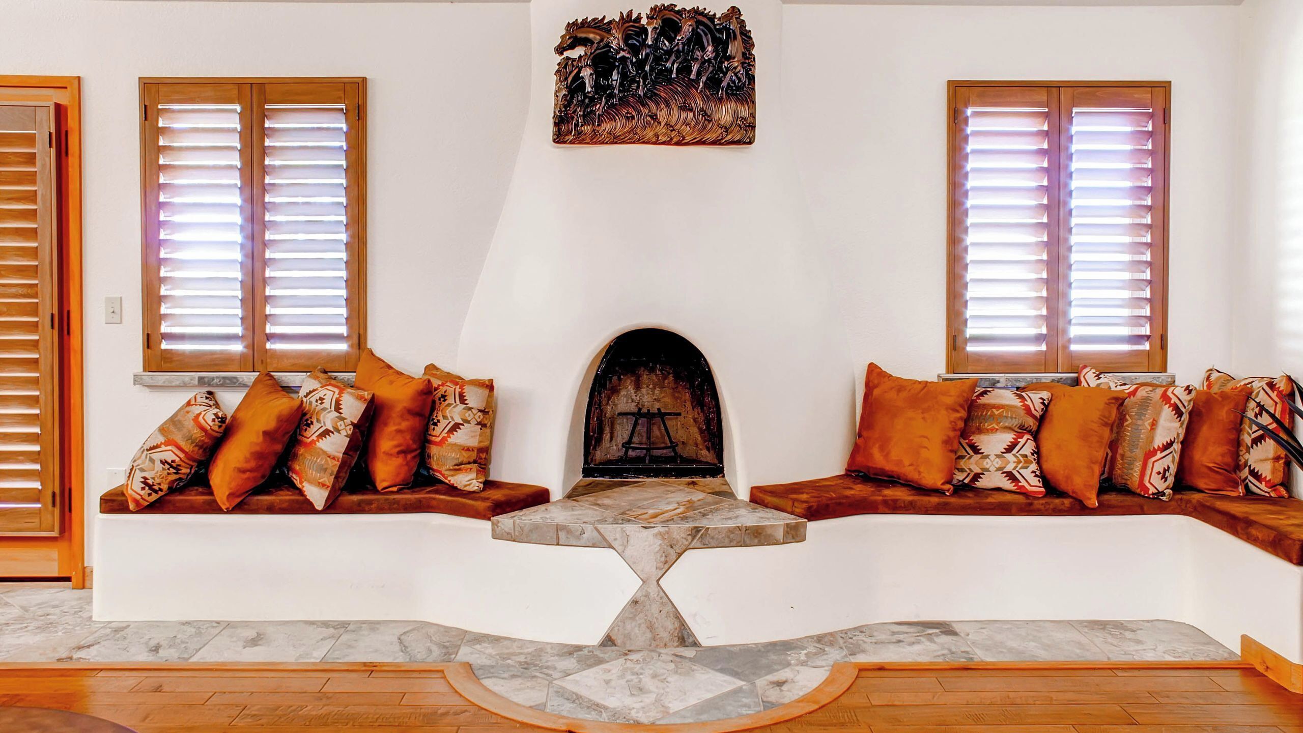 Una sala de estar acogedora con chimenea, dos ventanas con persianas y un sofá con cojines estampados.