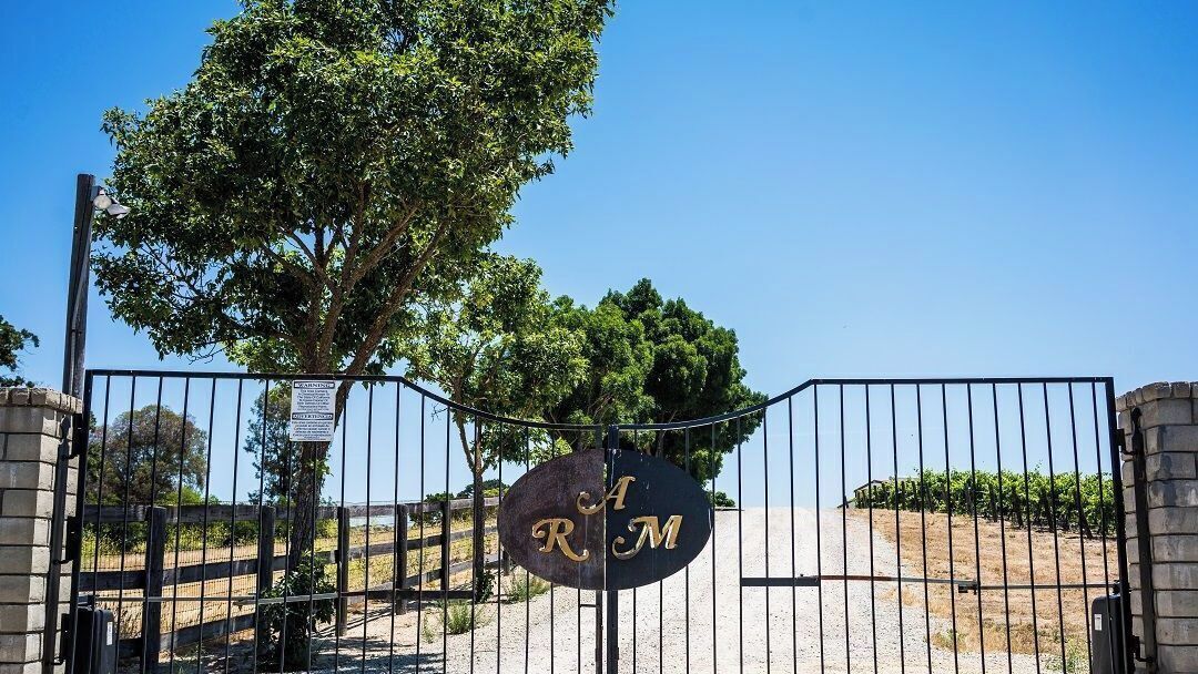 Una entrada con puerta de acceso y un letrero que dice 'R M', con un árbol al fondo.