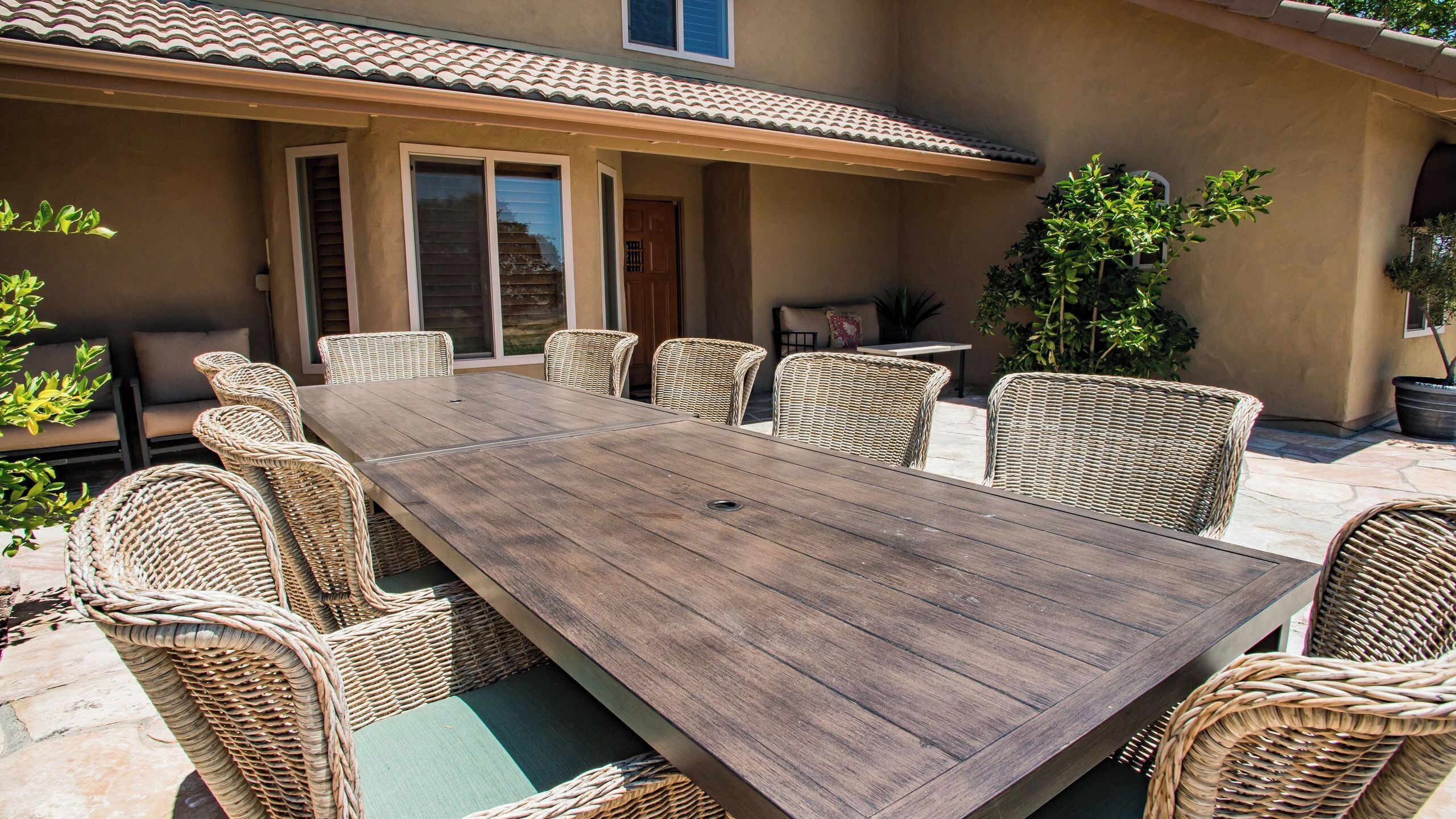 Un patio con una larga mesa de madera y sillas de mimbre.