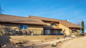 Un edificio residencial con techo de tejas, un patio cercado con mobiliario exterior, y un cielo despejado.