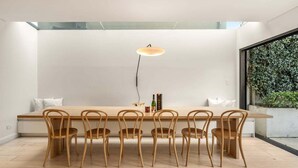 Un comedor con una mesa de madera larga y seis sillas, una lámpara colgante y vistas a la vegetación a través de un ventanal grande.