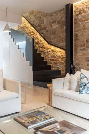 A modern interior with a staircase against a stone wall, a white sofa, and a magazine on a coffee table. - Palmer Darlinghurst - Stunning Terrace Home (Darlinghurst)