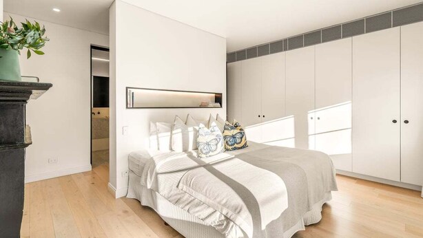 Un dormitorio con cama, mesita de noche, planta en maceta y un ventanal grande.