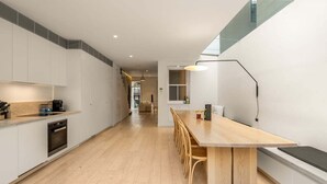 Una cocina moderna con una mesa de madera larga y sillas, un horno empotrado y una zona de comedor con banco.